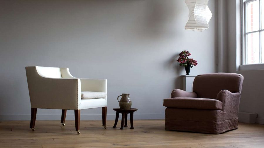 two armchairs on wood floor with side table and jug with vase of flowers by window