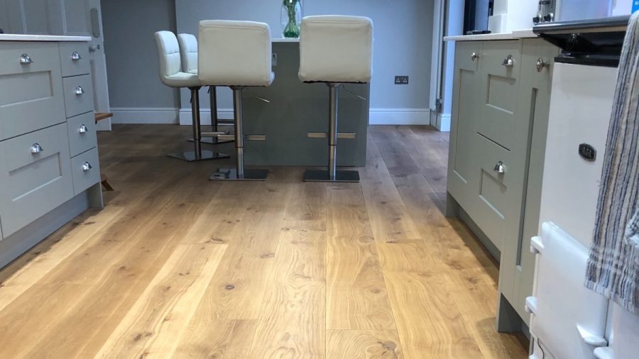 engineered ash wood flooring in kitchen with pale green cabinets and island with whie leather chairs