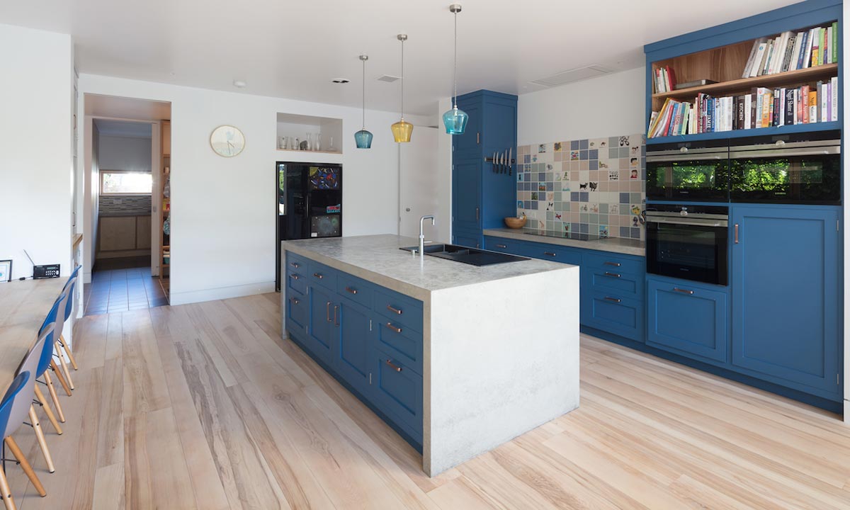 blue kitchen with marble topped island built in ovens and bookcase above