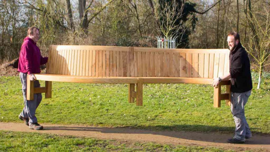 serpentine bench seat being carried by two men in a park