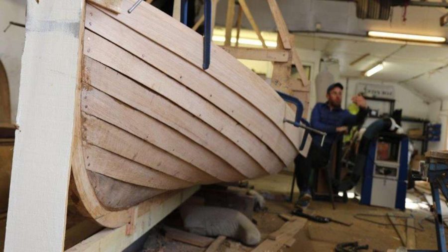 side view of boat with overlapping boards and workman in a shed