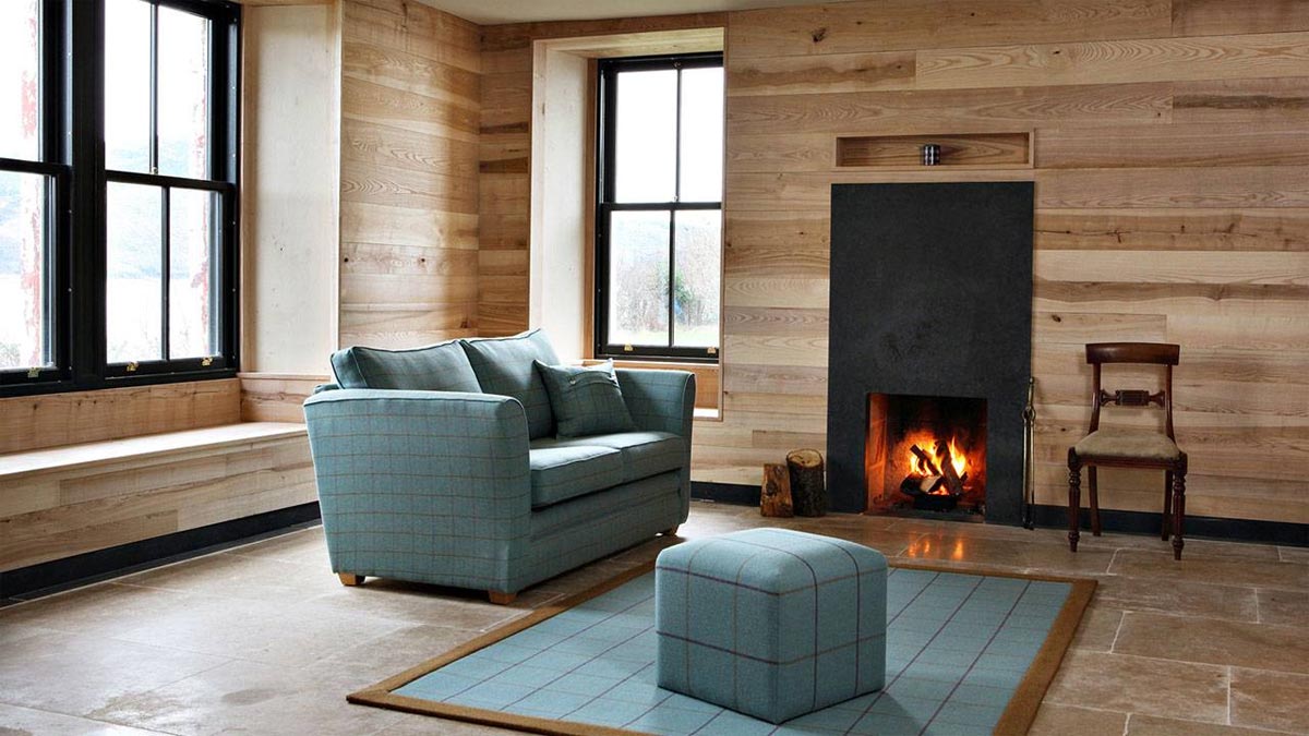wood clad walls and stone floor with pale blue tartan style sofa and footstool with roaring fire