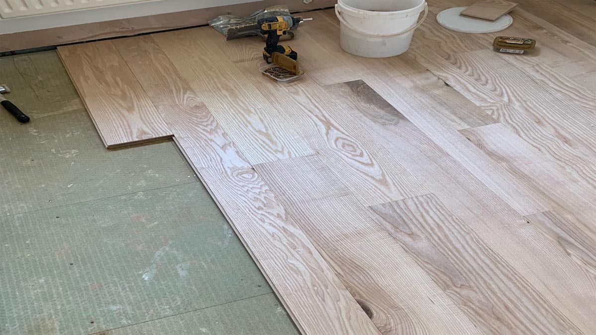 laying engineered wood flooring board on concrete screed with tools