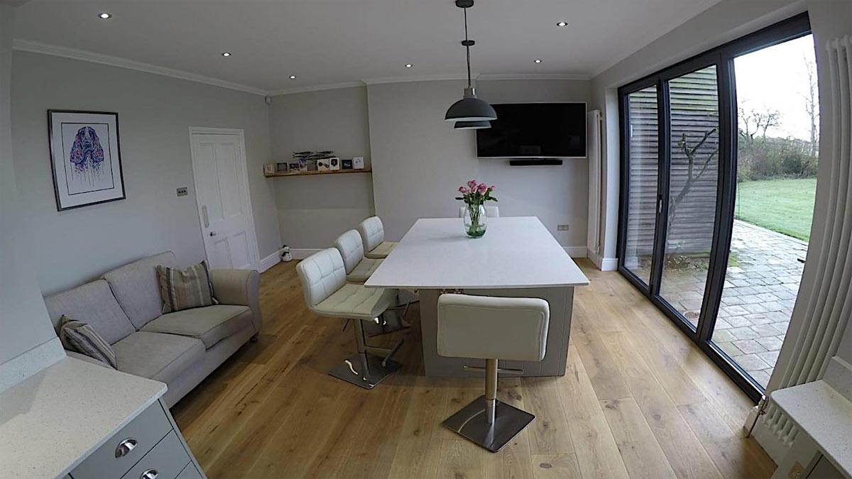 large kitchen island with padded white chairs and bi fold doors to garden
