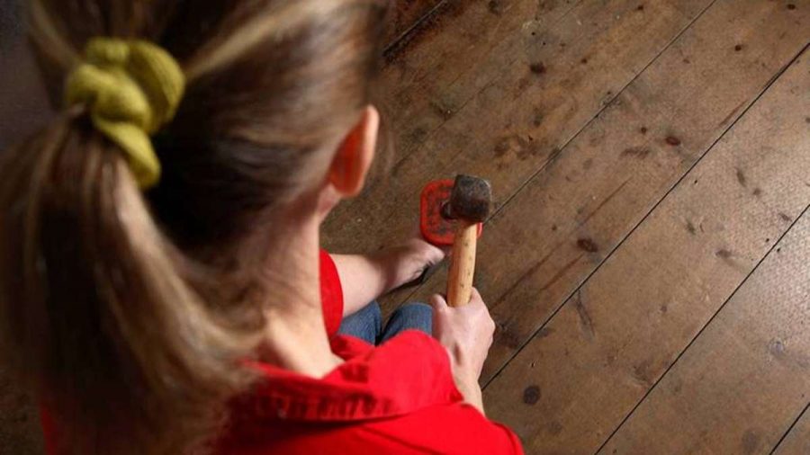 girl with hammer knocking nail in wood floor