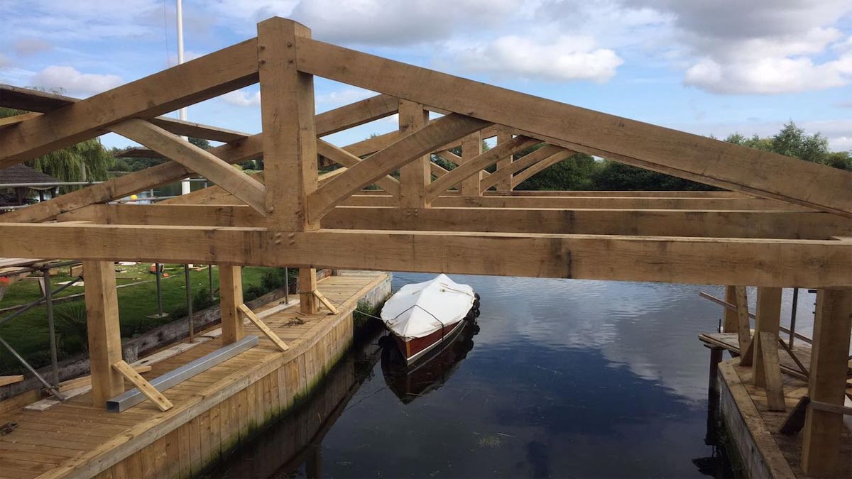 structural queen oak beams over boat house on river with boat moored up