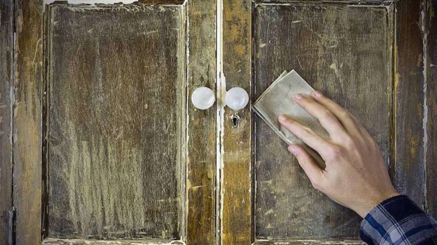 persons hand sandpapering old cupboard doors